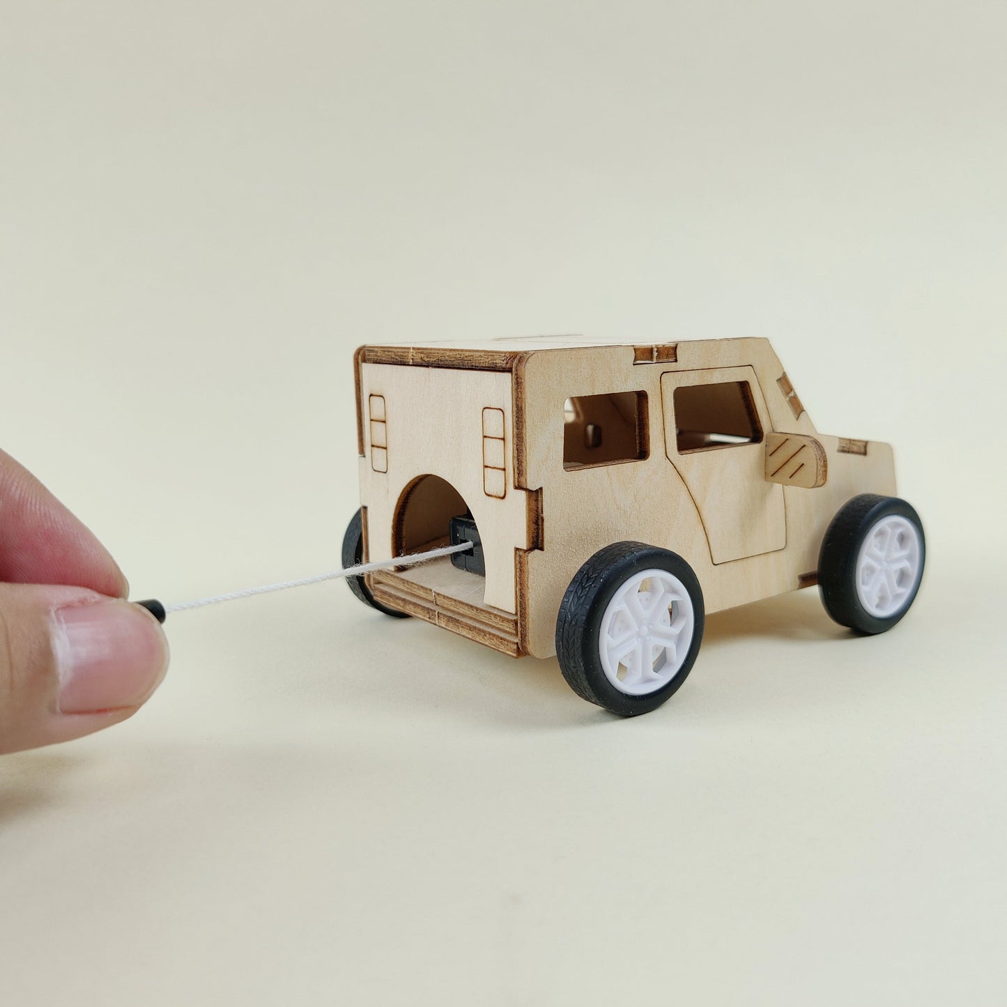 Small wooden model of a vehicle on wheels with a hand holding a string.