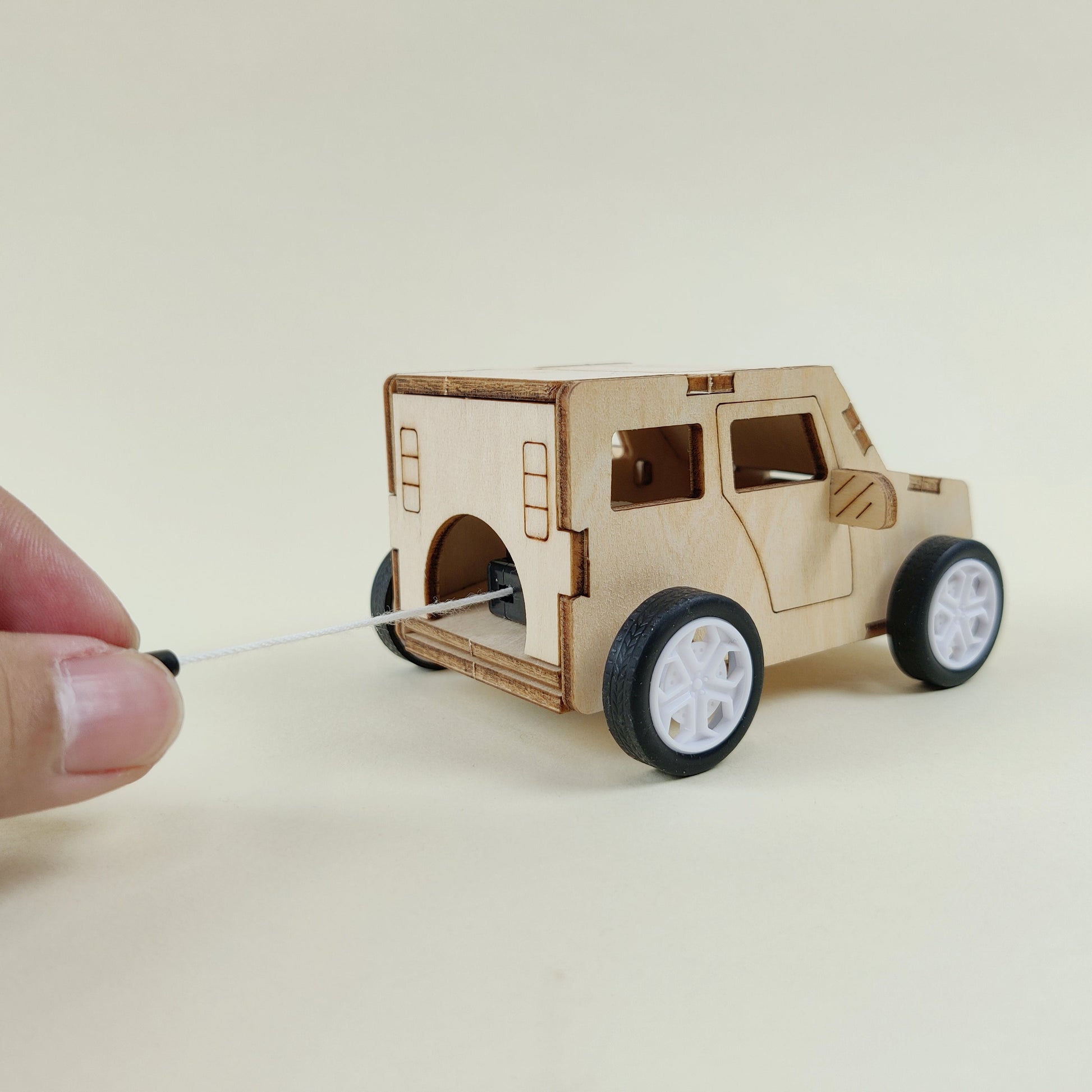 Small wooden model of a vehicle on wheels with a hand holding a string.