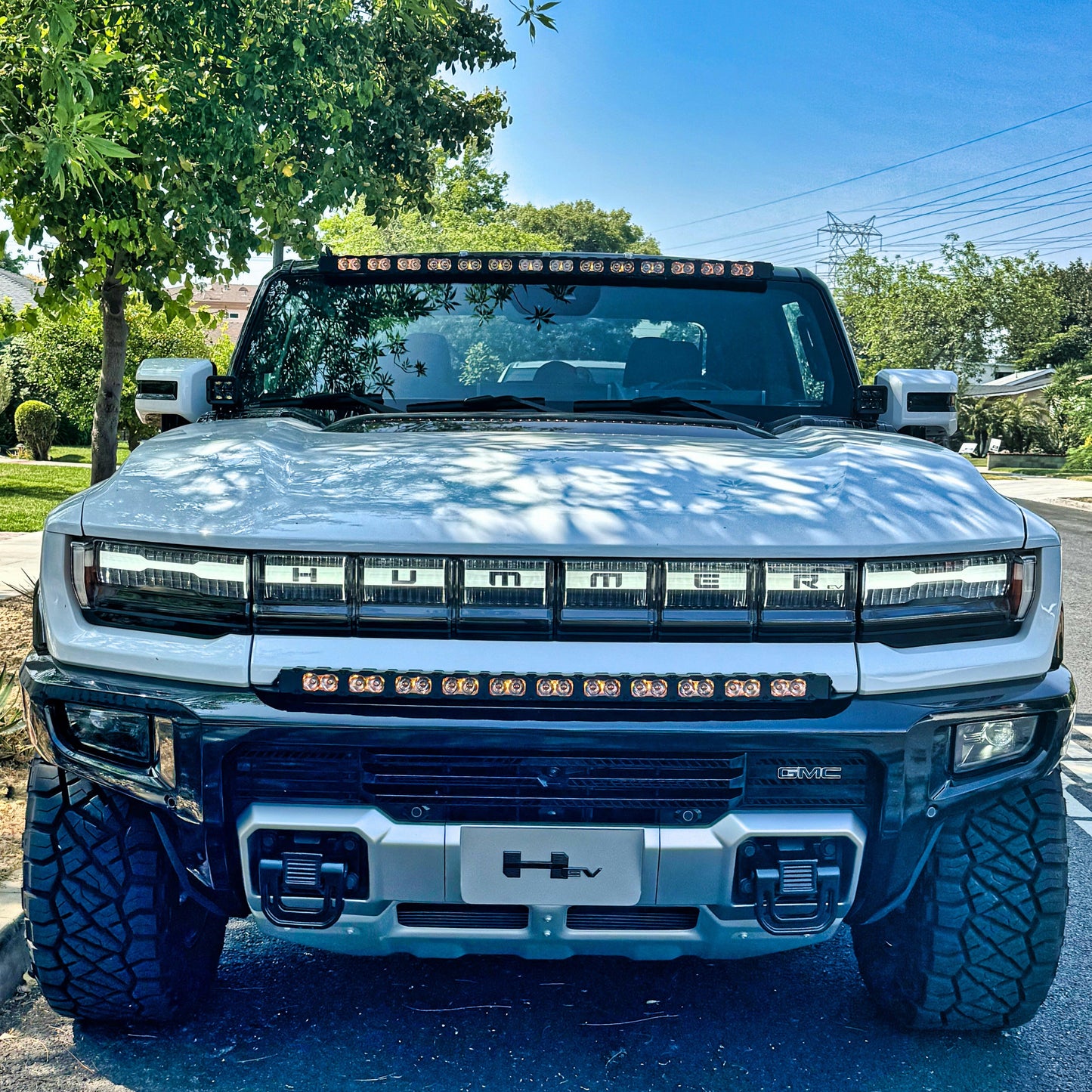 Front view of a white Hummer truck on a road with trees and power lines in the background.
