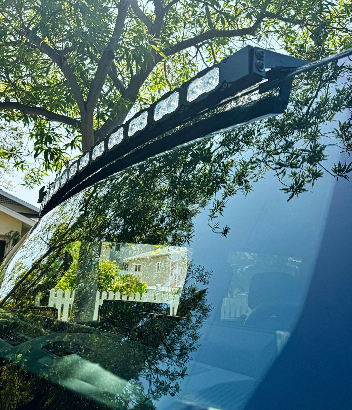 Car roof rack with lights on a vehicle, reflecting trees and house.