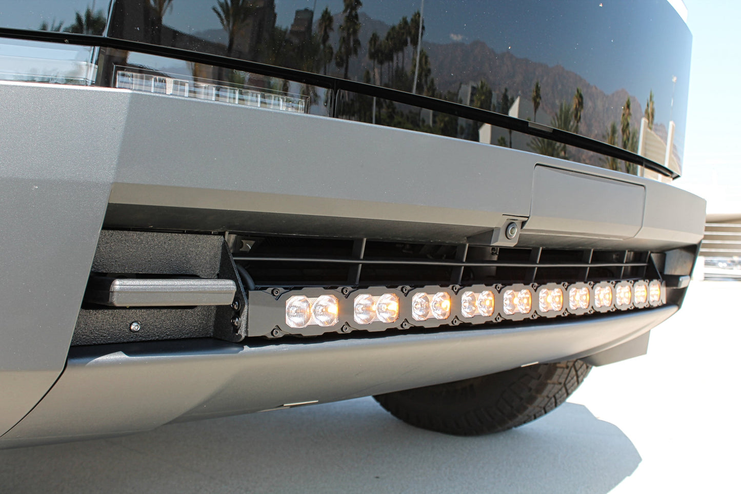 Close-up of a vehicle's front bumper with LED lights, set against a mountainous landscape.