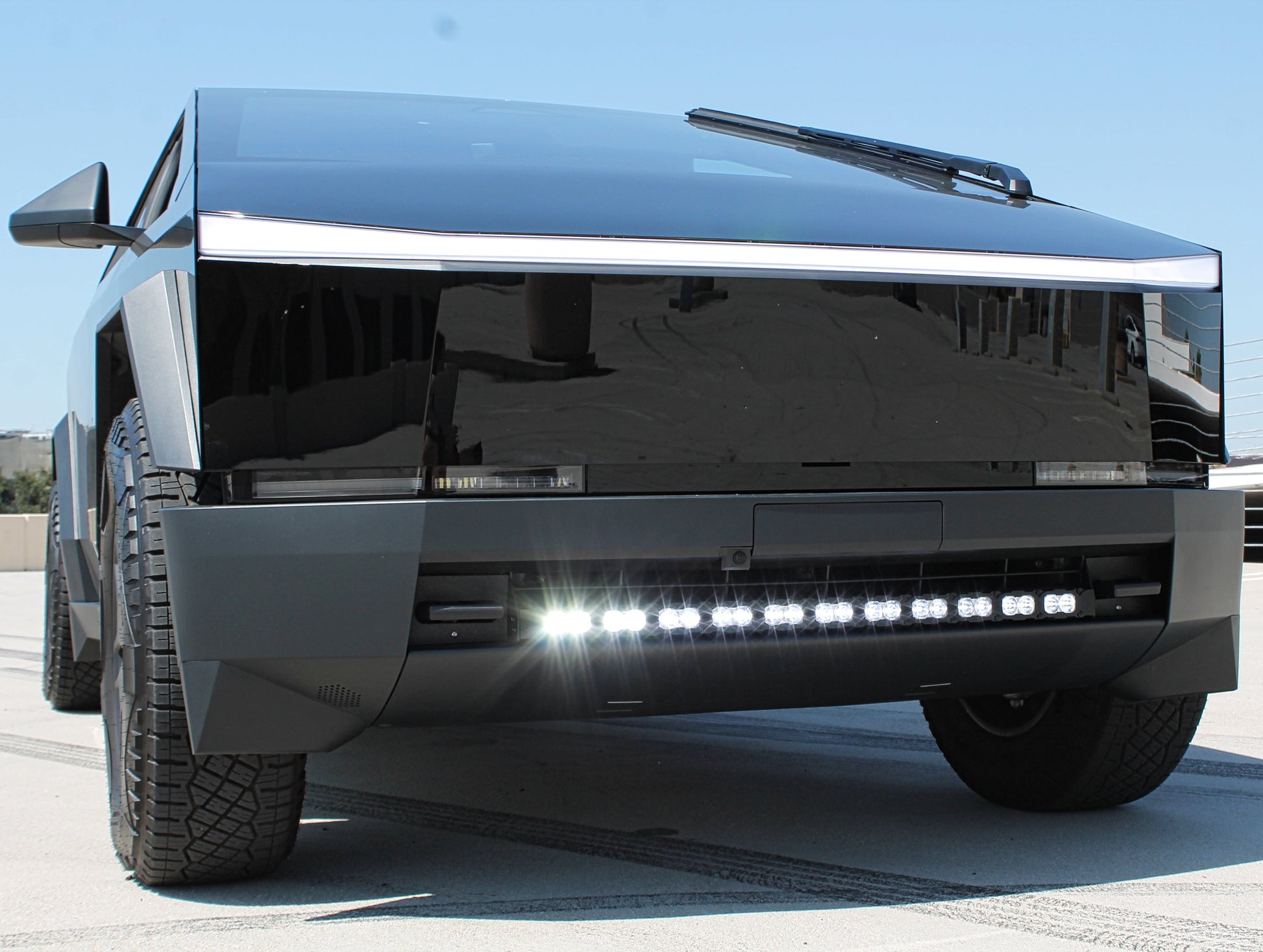 Front view of a black tesla truck with large headlights on a clear day.