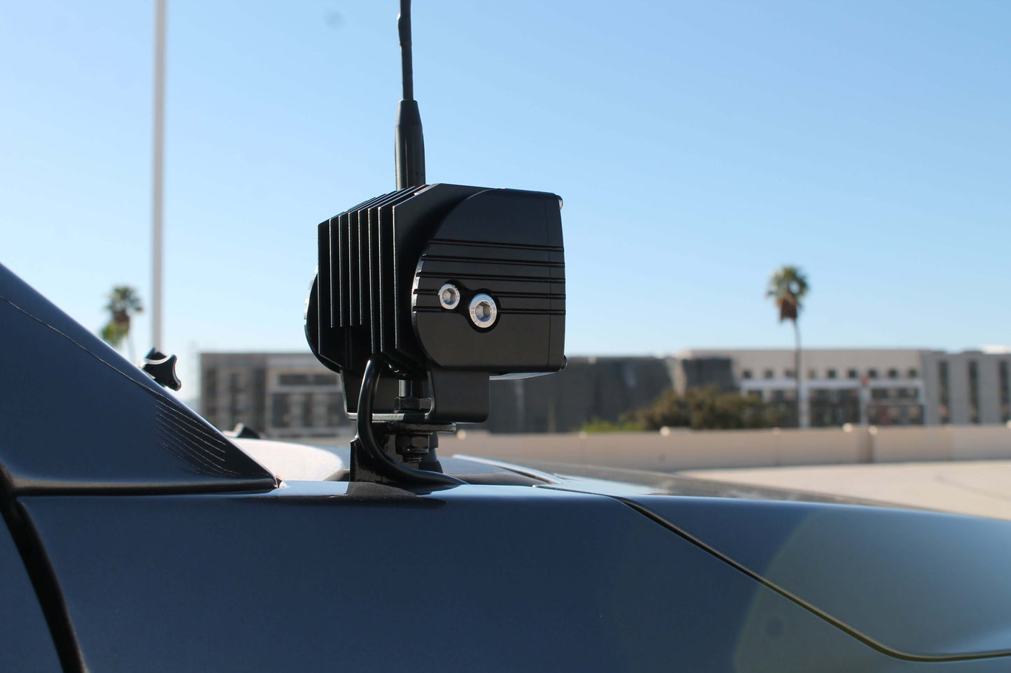 Black antenna and mounted Hood Light on a car with a clear blue sky background