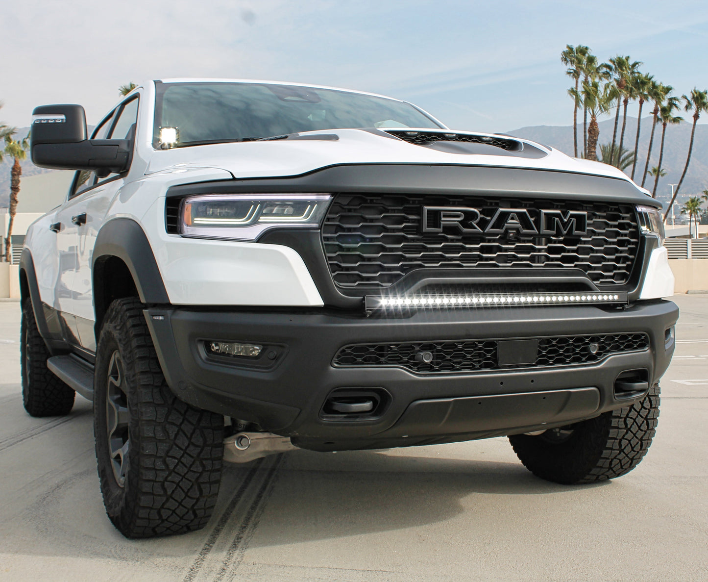 White Ram truck with black grille and LED light bar on a concrete surface with palm trees in the background.