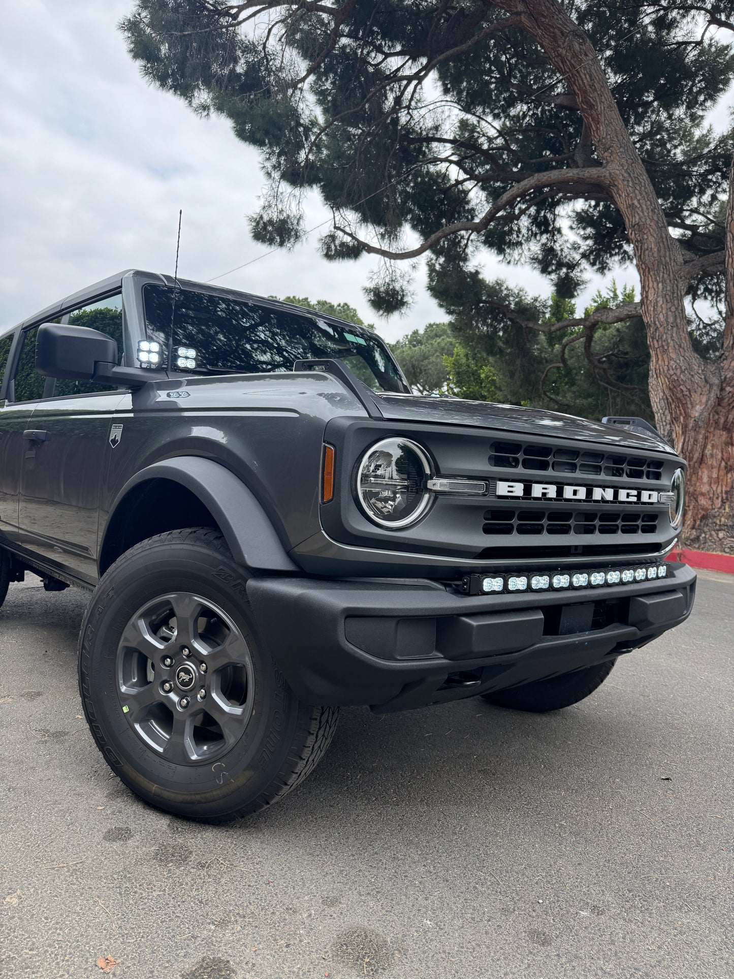 Gray Ford Bronco truck with LED Light bar parked on a street with trees in the background