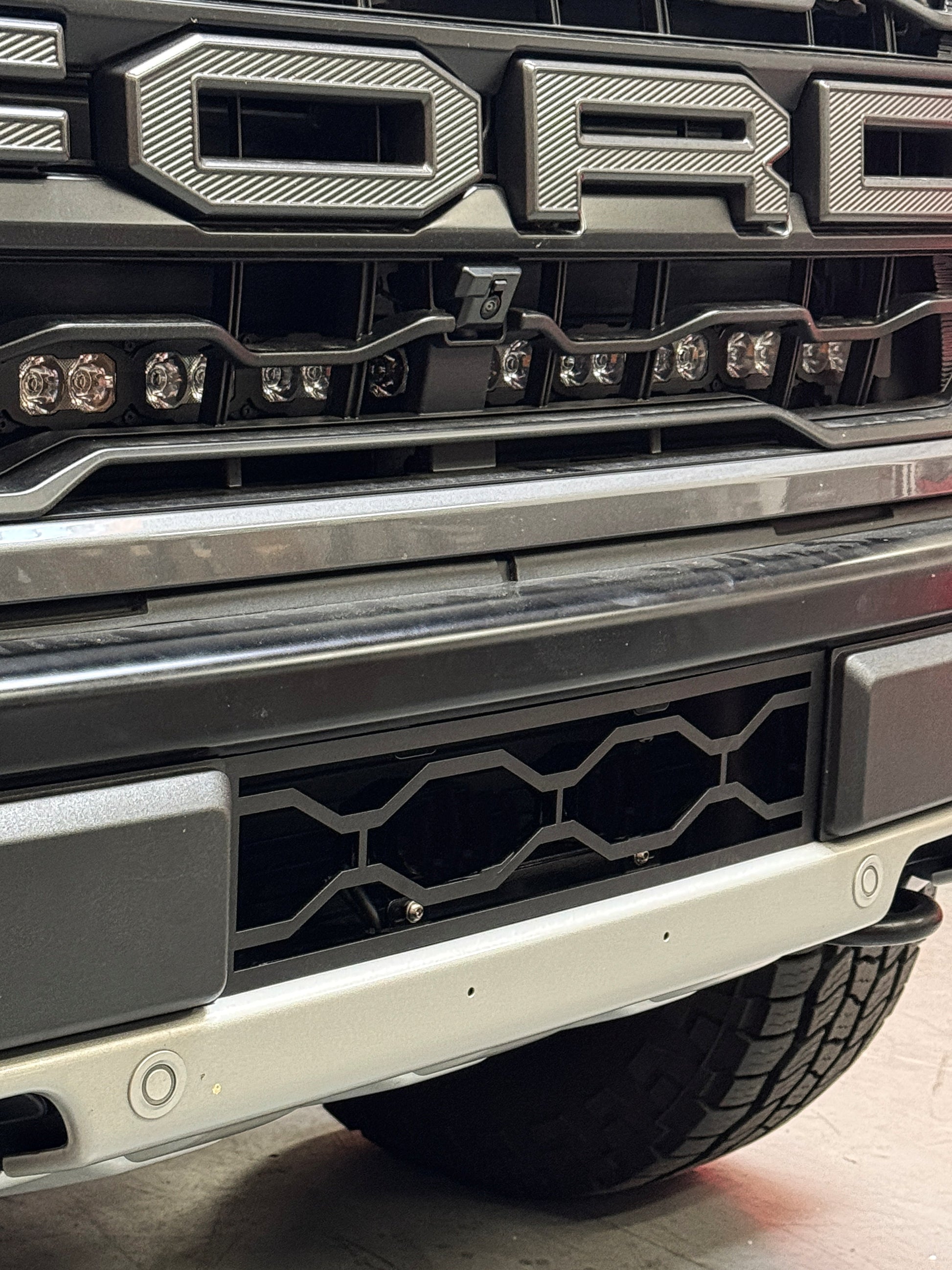 Close-up of a vehicle grille with 'Ford' branding and Ford Raptor Gen 3 Refresh Guard Plate