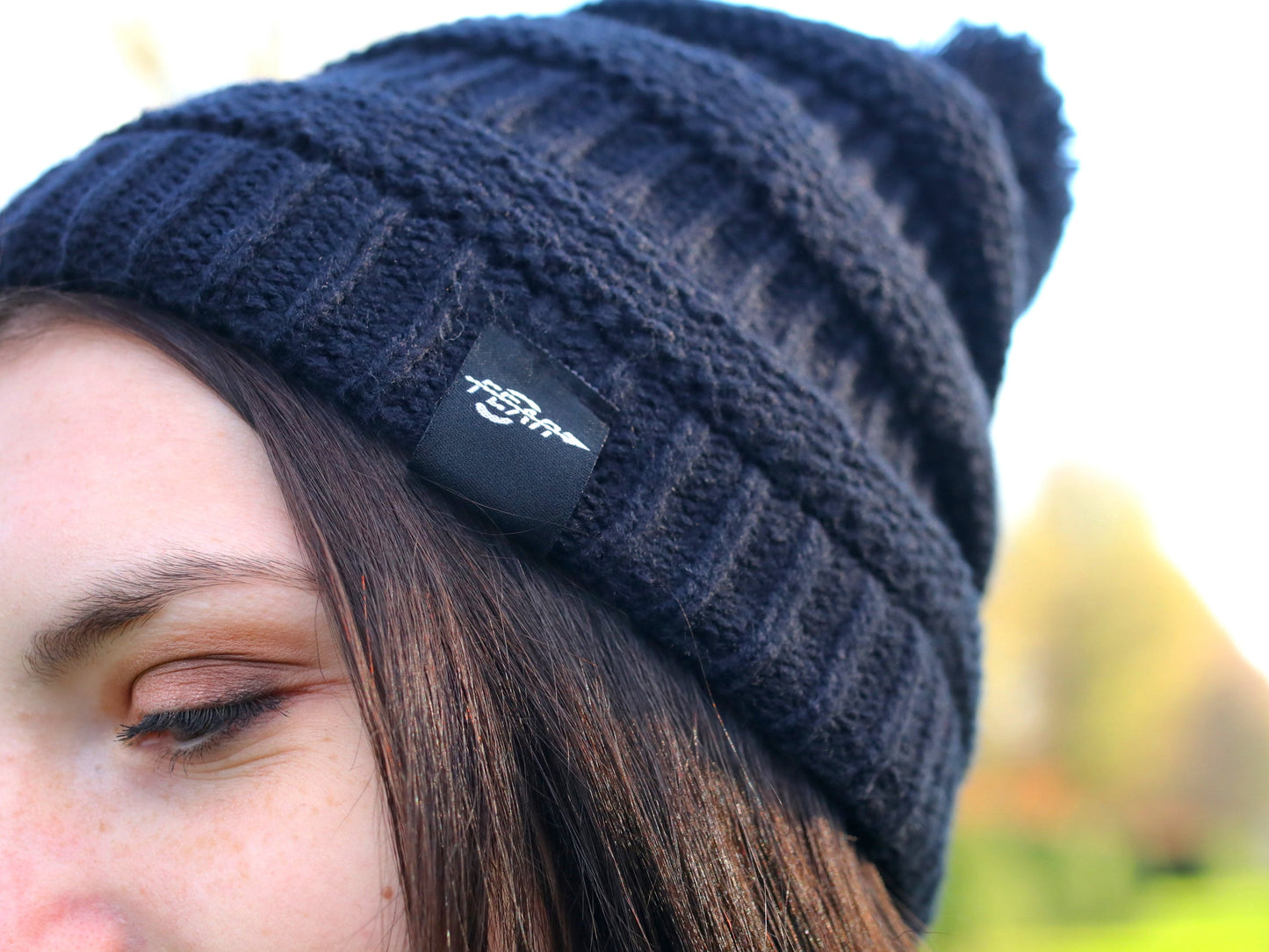 Navy blue knit beanie with a brand logo worn by a person outdoors.
