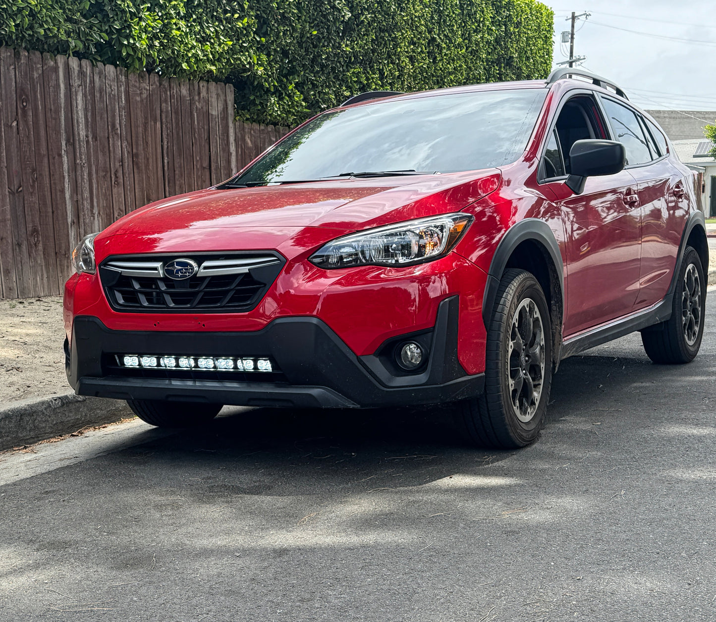Red SUV parked on a street with a wooden fence and greenery in the background