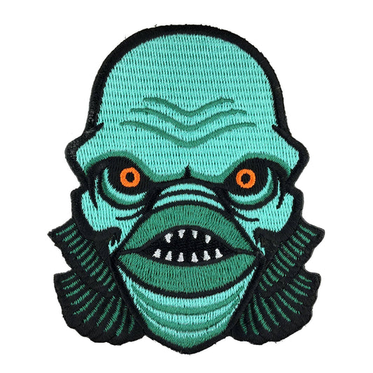 Embroidered patch of a green creature with orange eyes on a white background