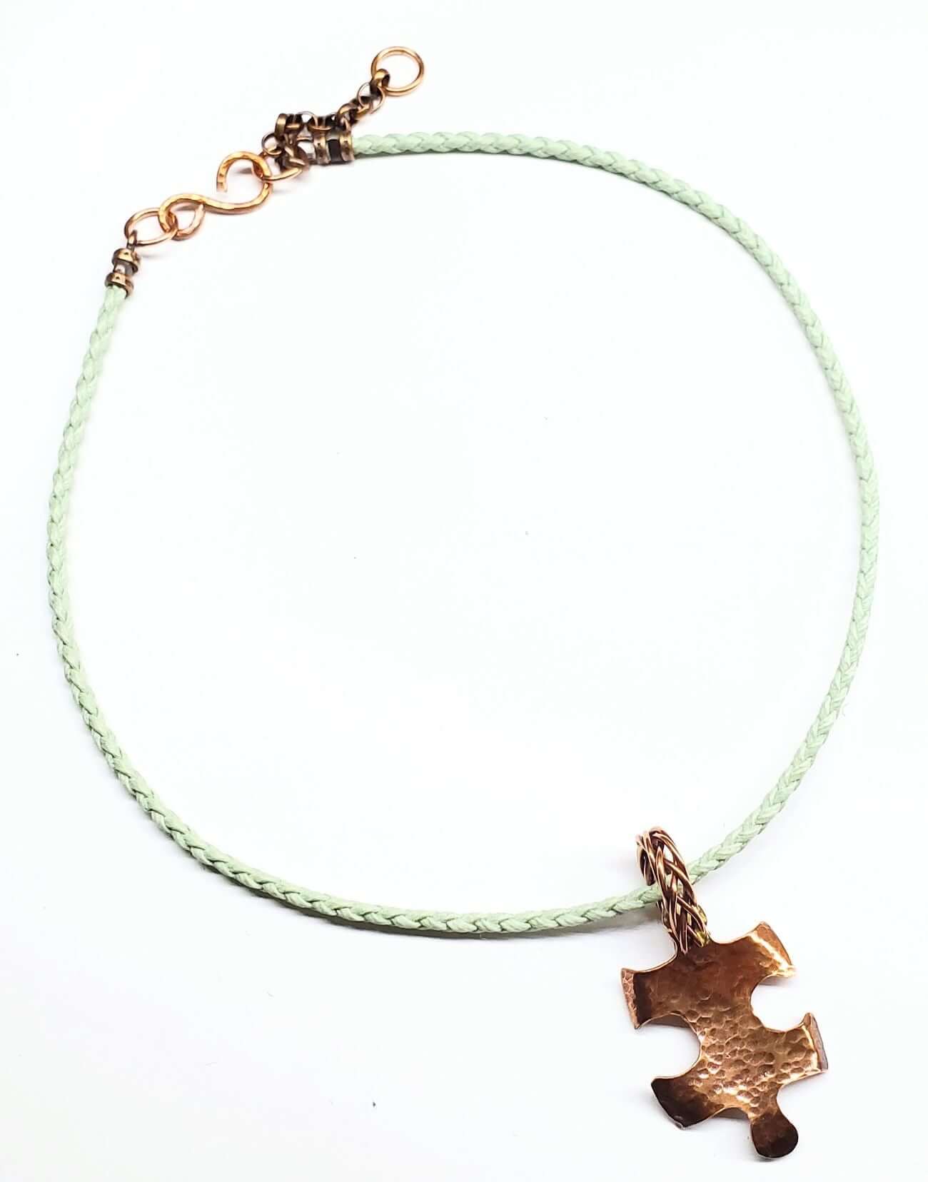 Autism Necklace with a green cord and bronze puzzle piece pendant on a white background
