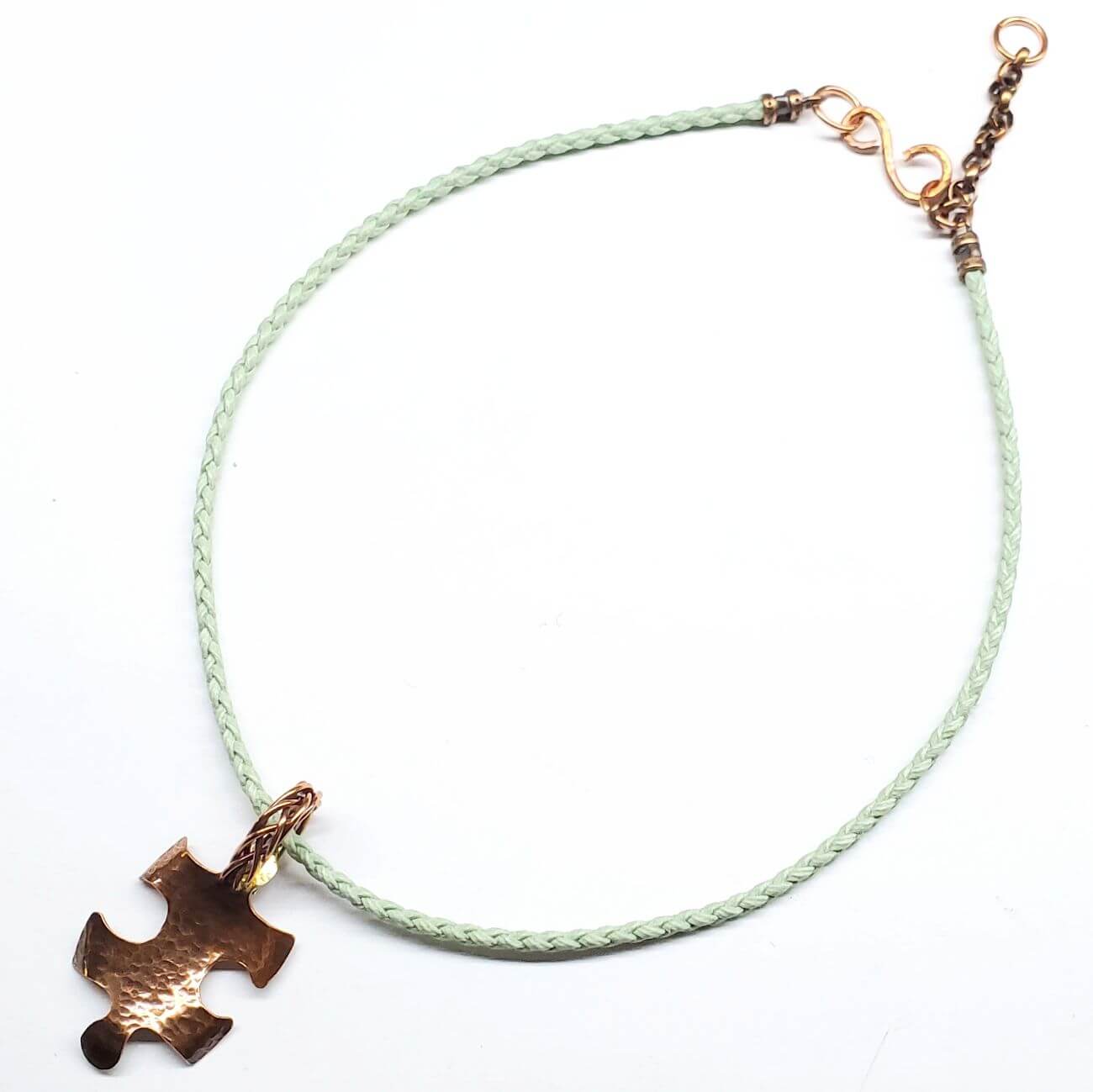 AUtism awareness Necklace with a puzzle piece pendant on a light green cord against a white background