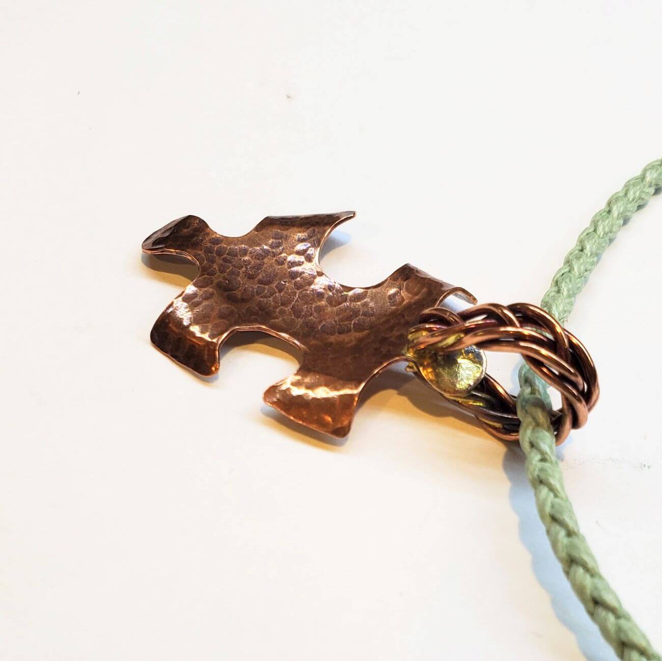 Copper puzzle piece charm on a green cord against a white background