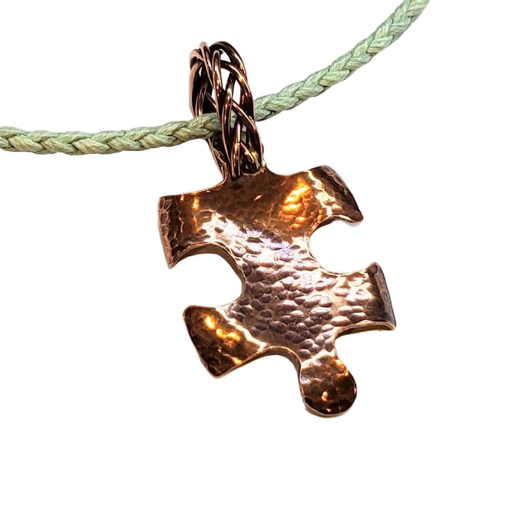 Bronze puzzle piece pendant on a green cord against a white background