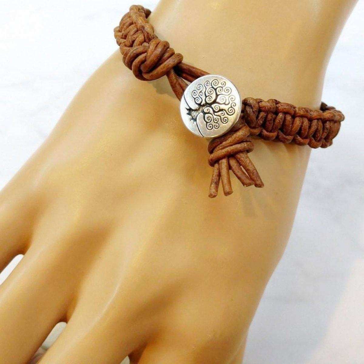 Brown braided bracelet with a silver tree-of-life button on a wrist against a white background