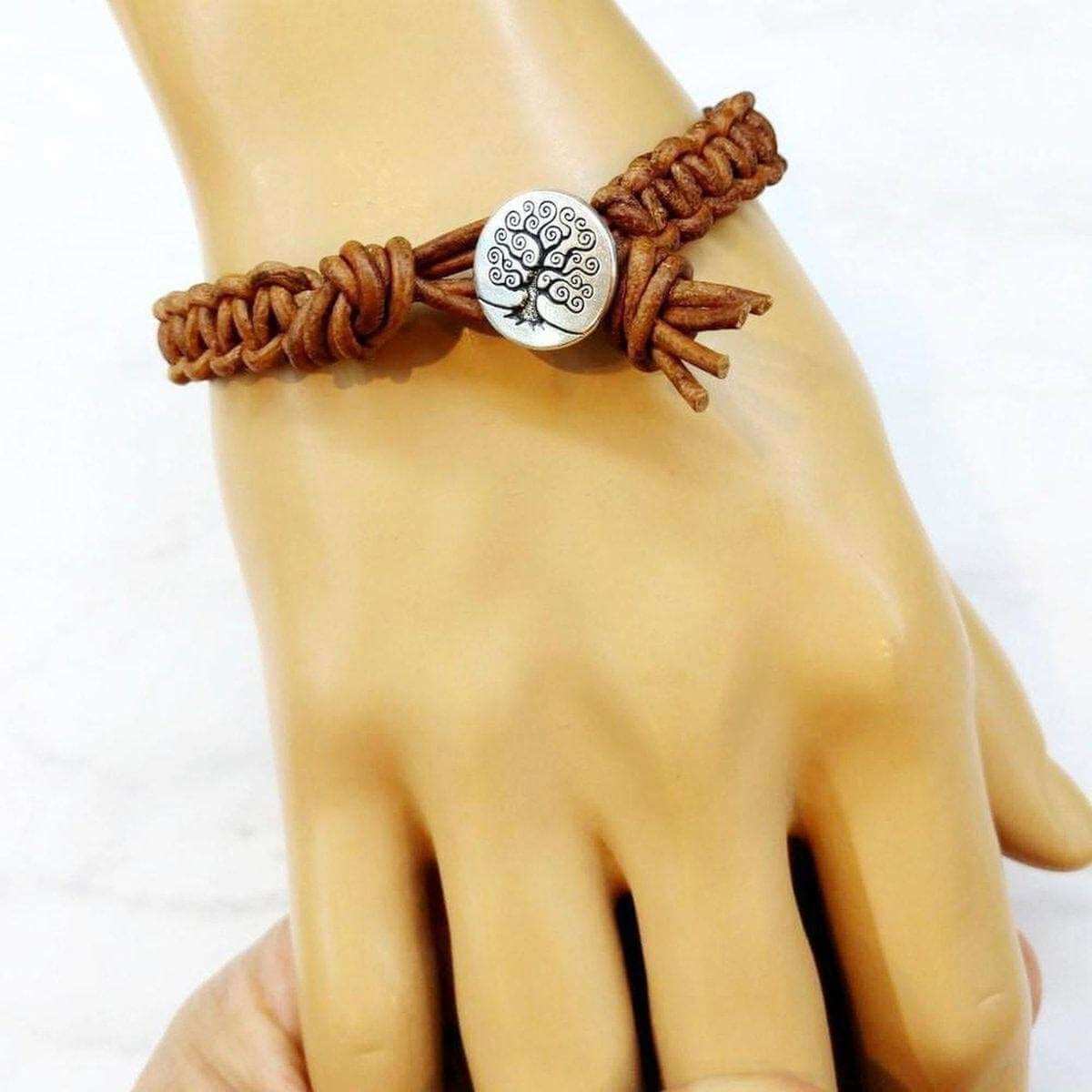 Brown braided bracelet with a silver tree-of-life charm on a hand against a white background