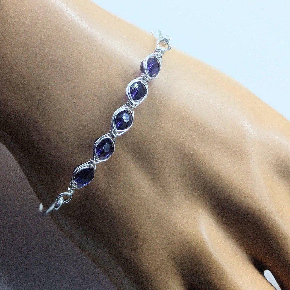Silver bracelet with purple stones on a wrist against a neutral background