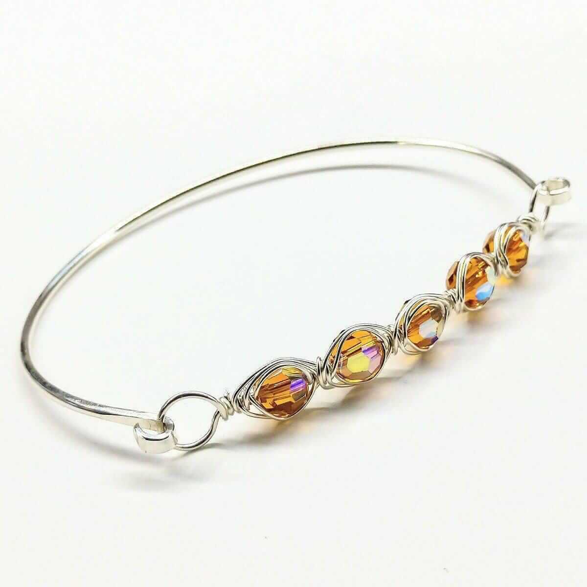 Silver bangle with orange gemstones on a white background