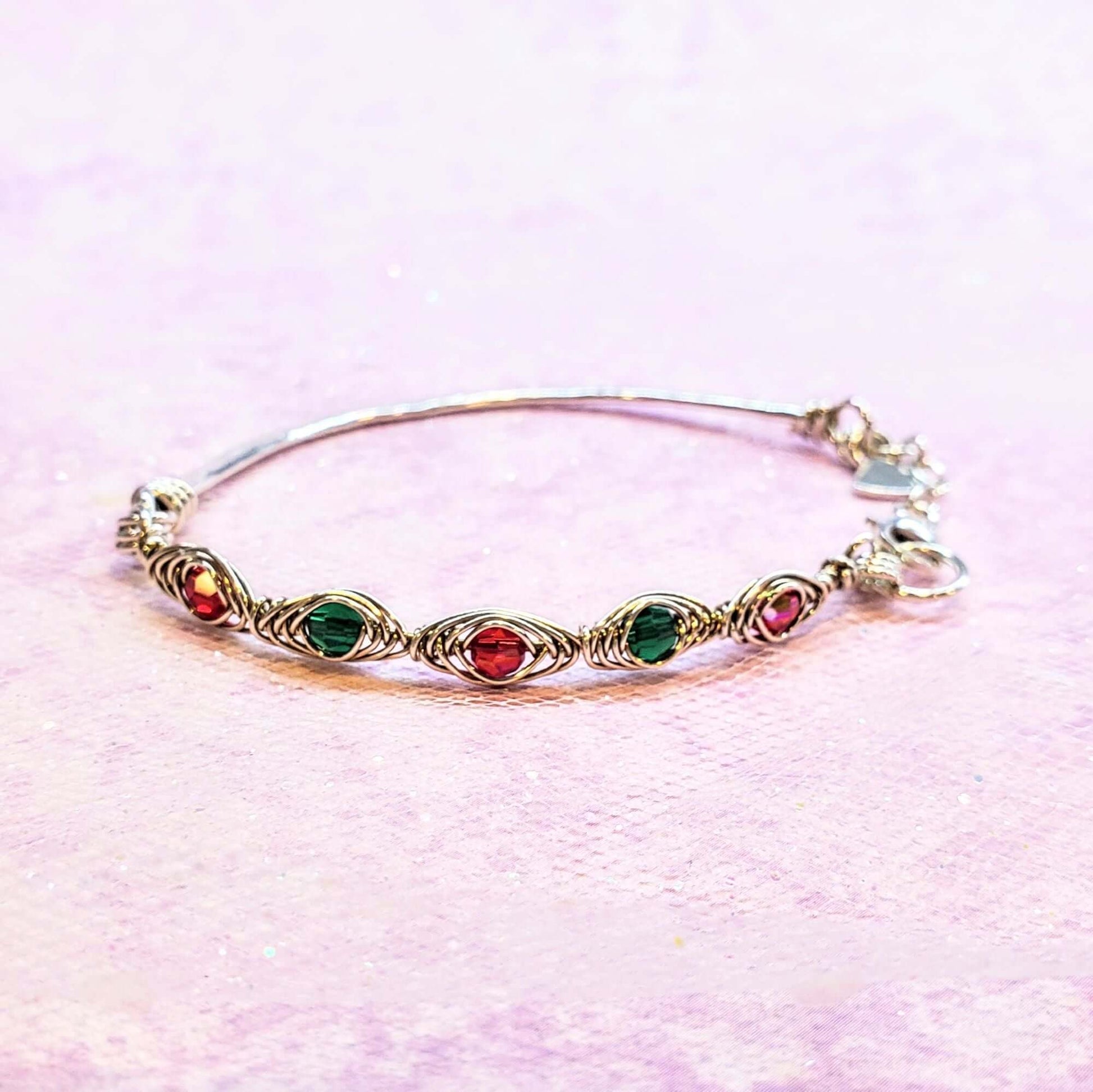 Gold bracelet with red and green gemstones on a pink background