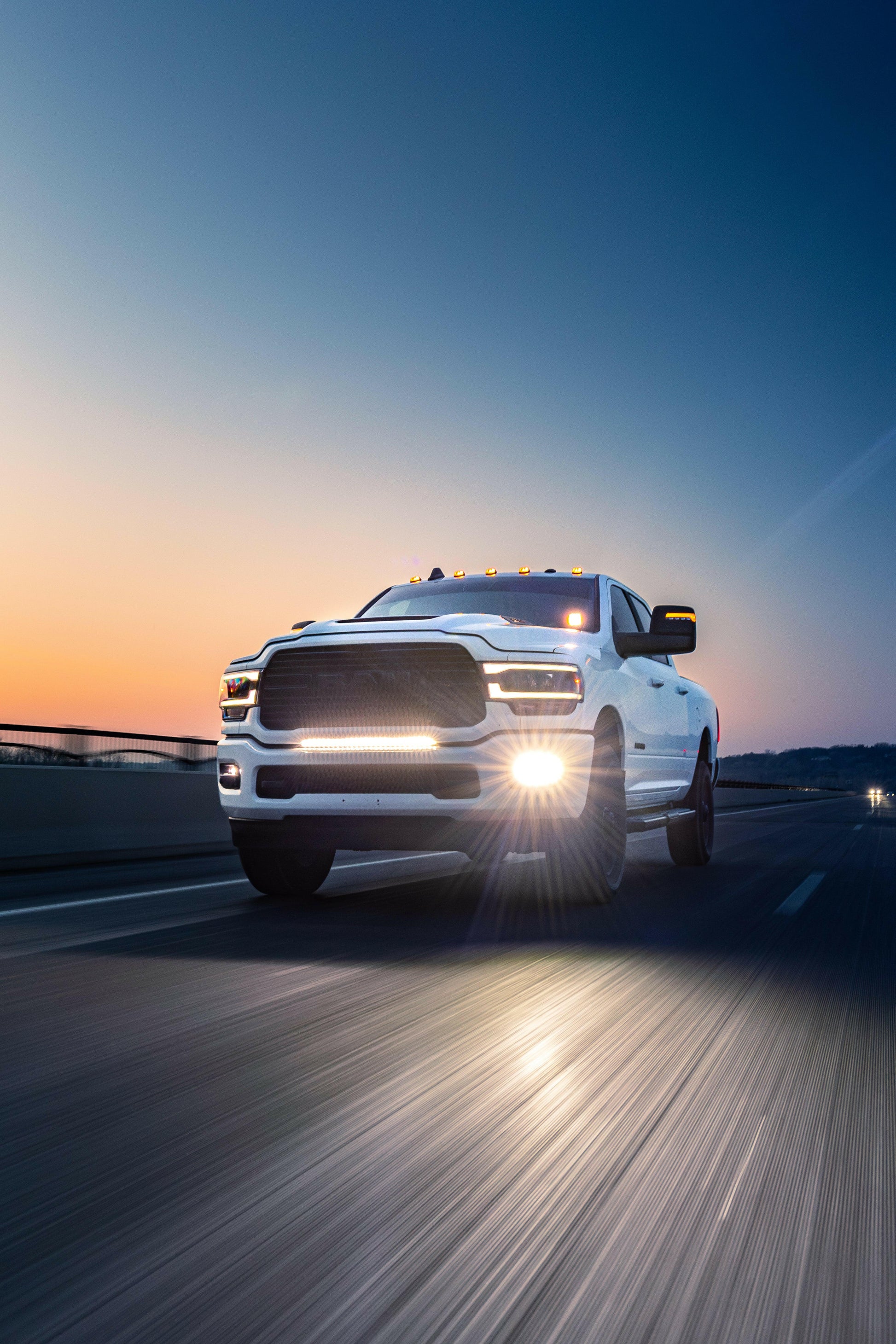 White pickup truck driving on a road with a sunset or sunrise in the background