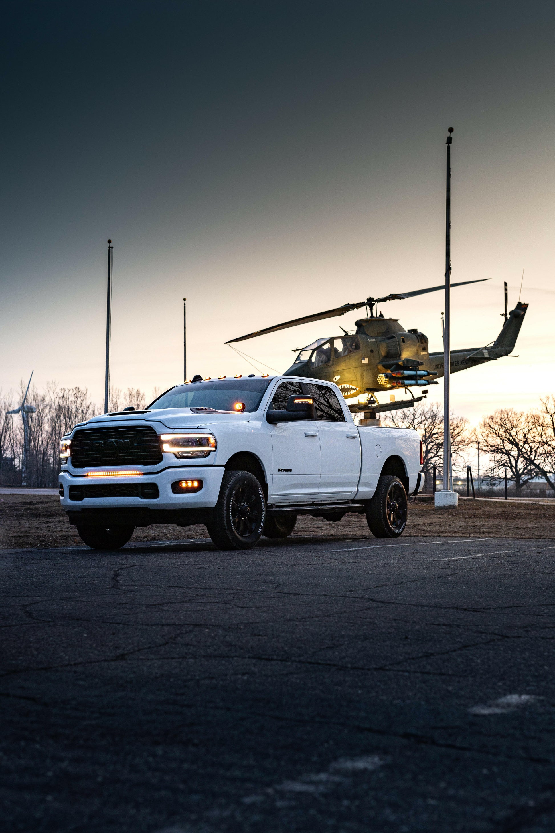 White Dodge pickup truck with LED Light bar and a helicopter in the background at dusk.