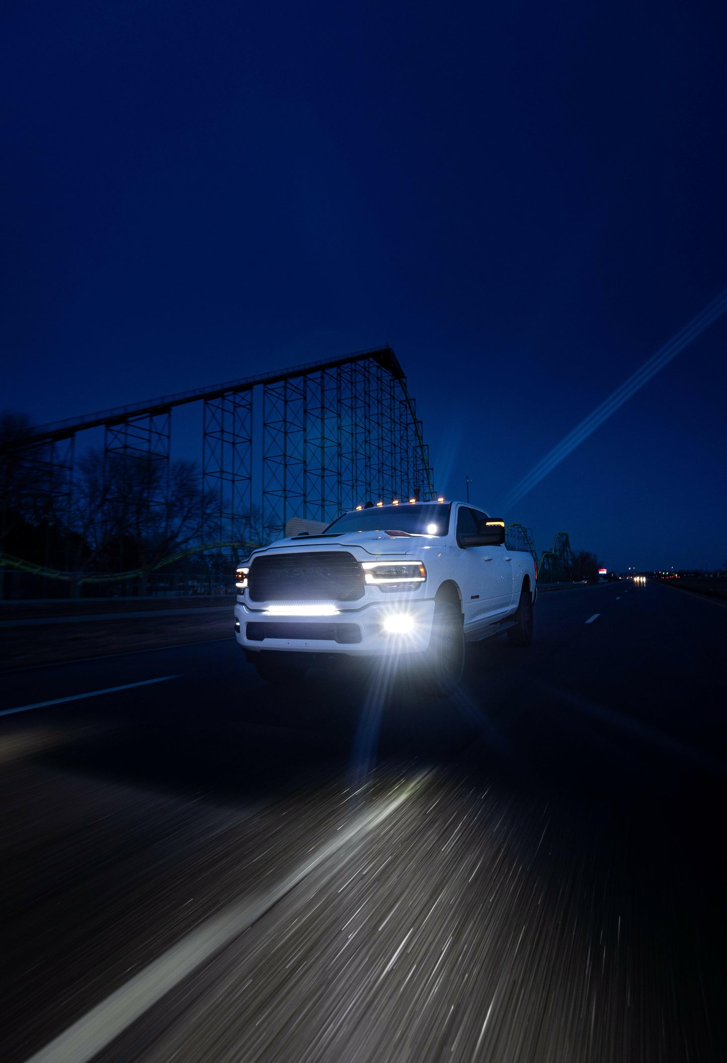 White pickup truck with bright headlights and light bar on a dark road at night