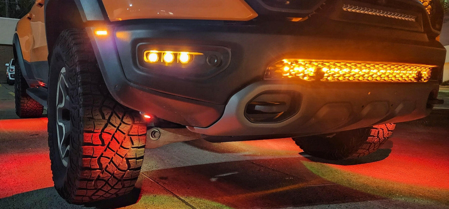 Close-up of a vehicle's front bumper with illuminated lights on a red-lit surface.