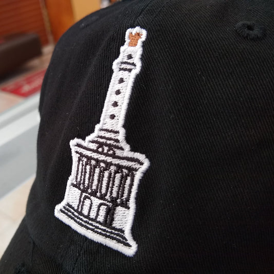 Black cap with a white embroidered design of a building on a blurred indoor background