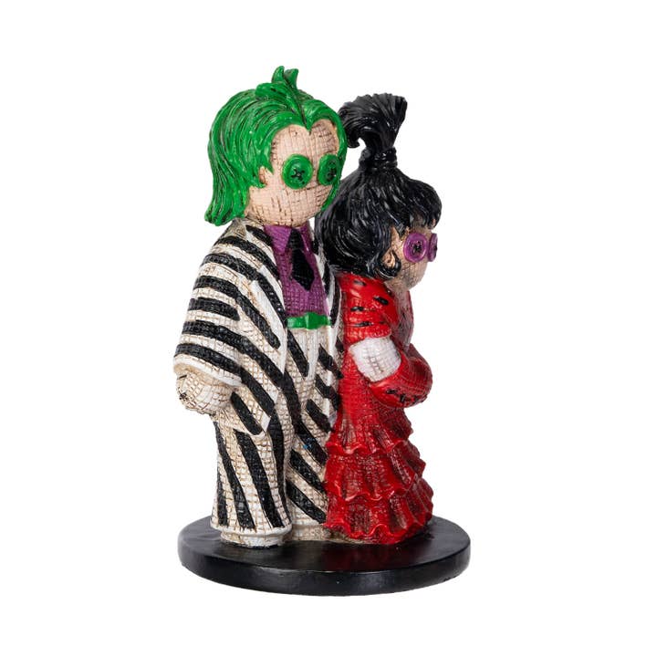 Statue of a character with green hair and zebra-striped suit standing next to a character with black hair and red dress on a white background.
