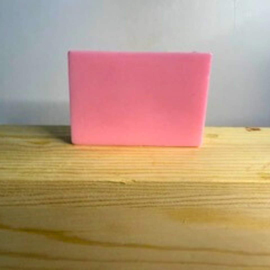 Pink bar of soap on a wooden surface with a light gray background