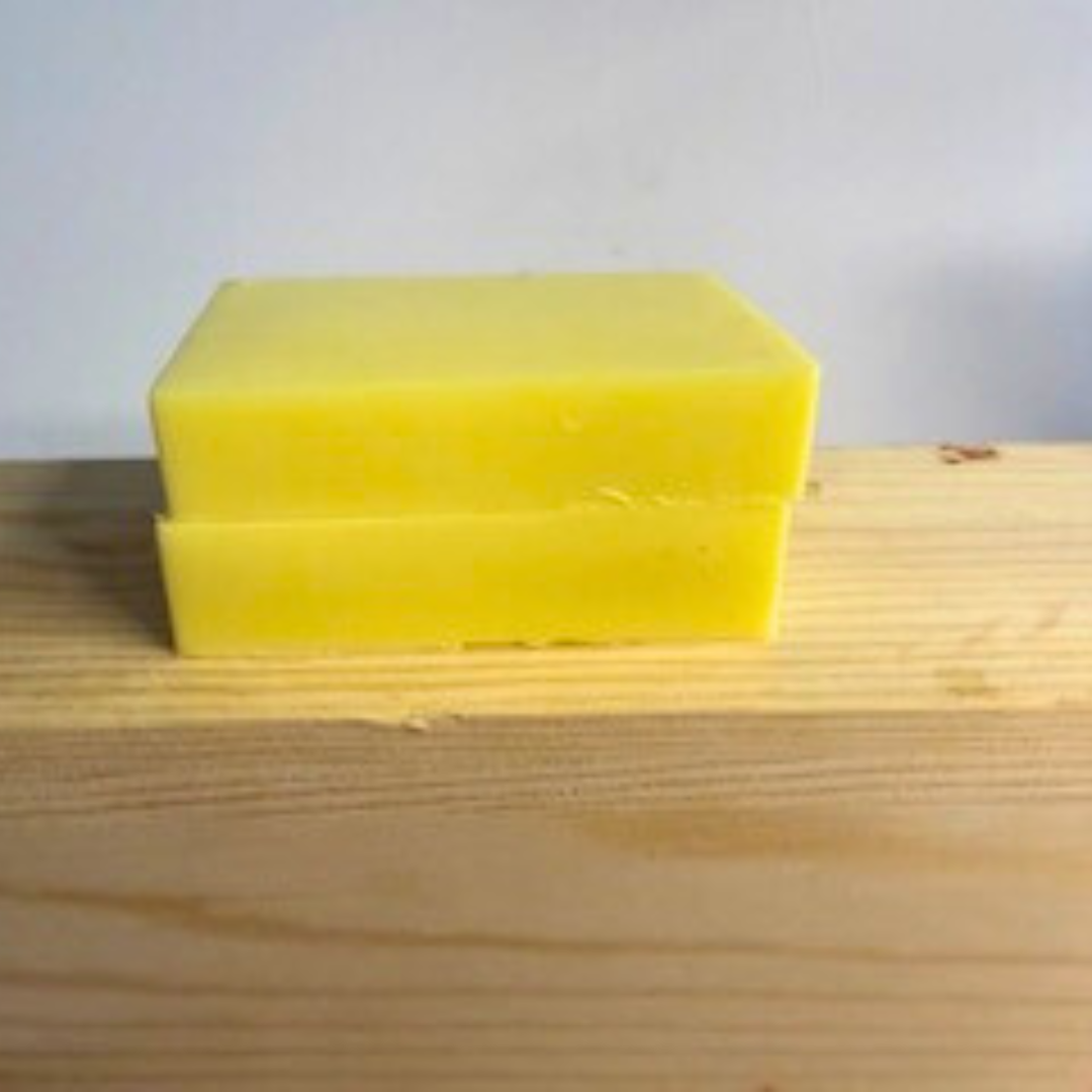 Two yellow Lemon Zest- Lemon Scented Handmade Soap blocks stacked on a wooden surface with a light gray background