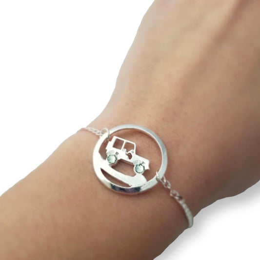 Silver bracelet with a circular design featuring a car and green gemstones on a wrist.
