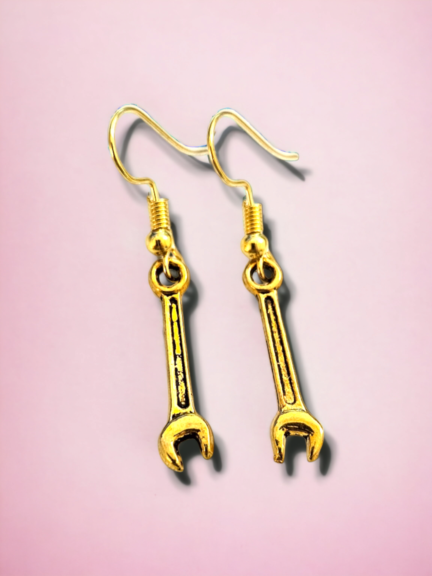 Gold wrench-shaped earrings on a pink background