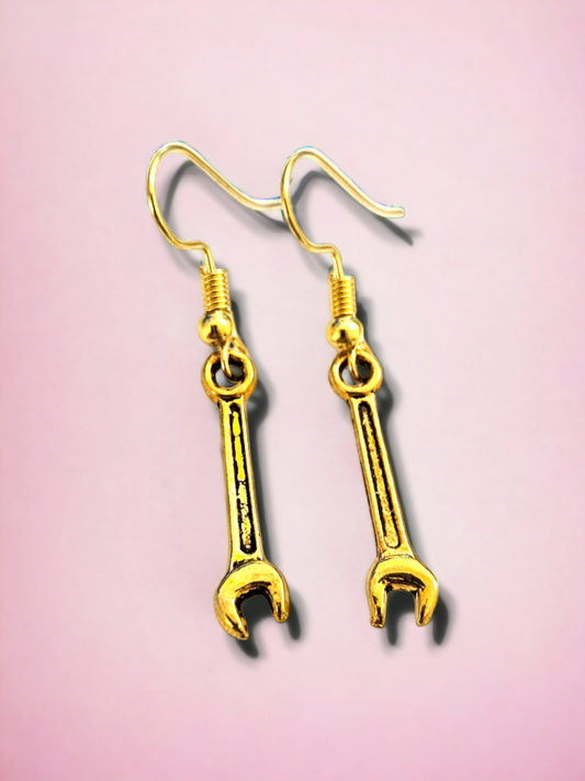 Gold wrench-shaped earrings on a pink background