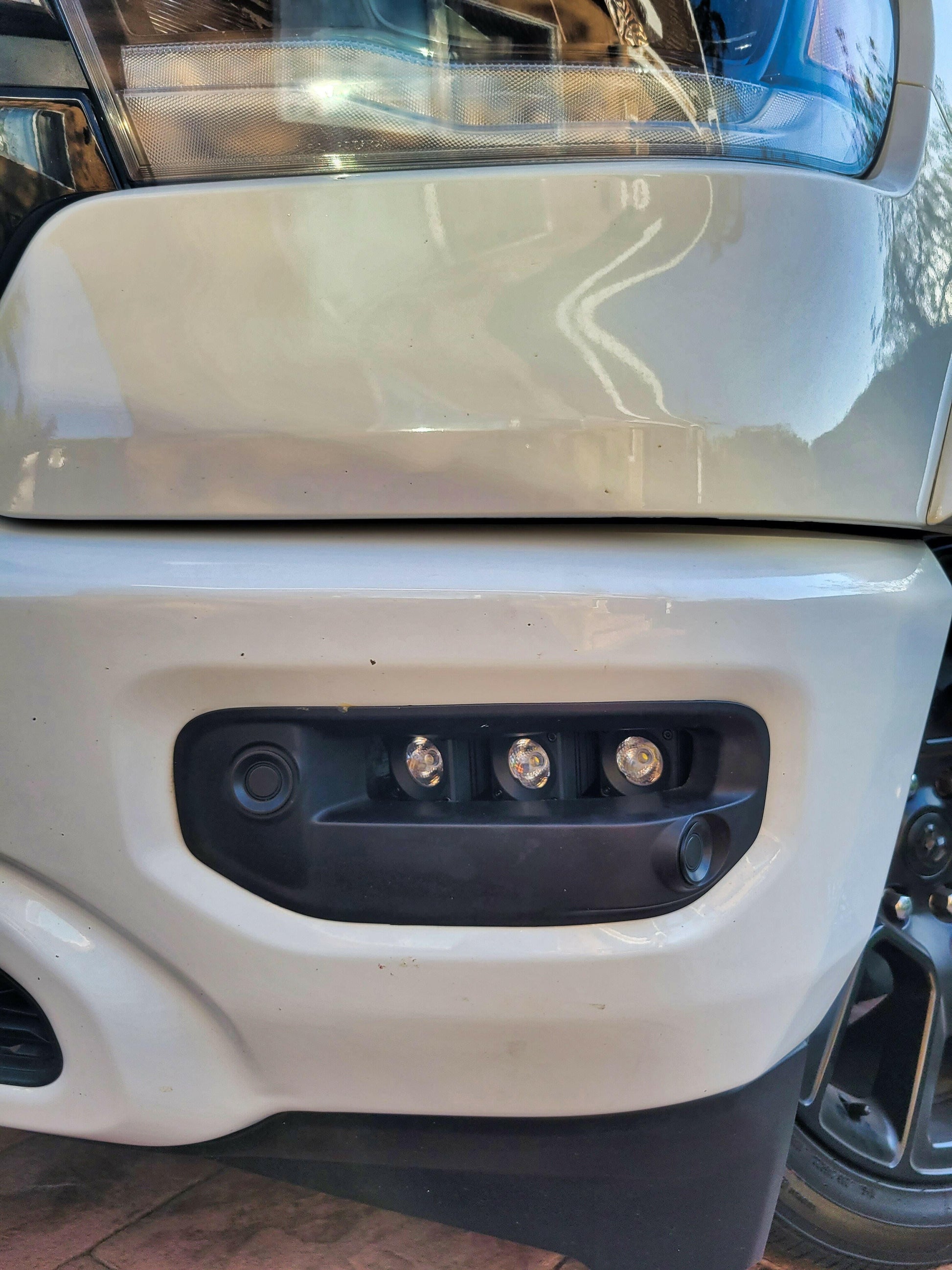 Close-up of a vehicle's front bumper with camera and lights.