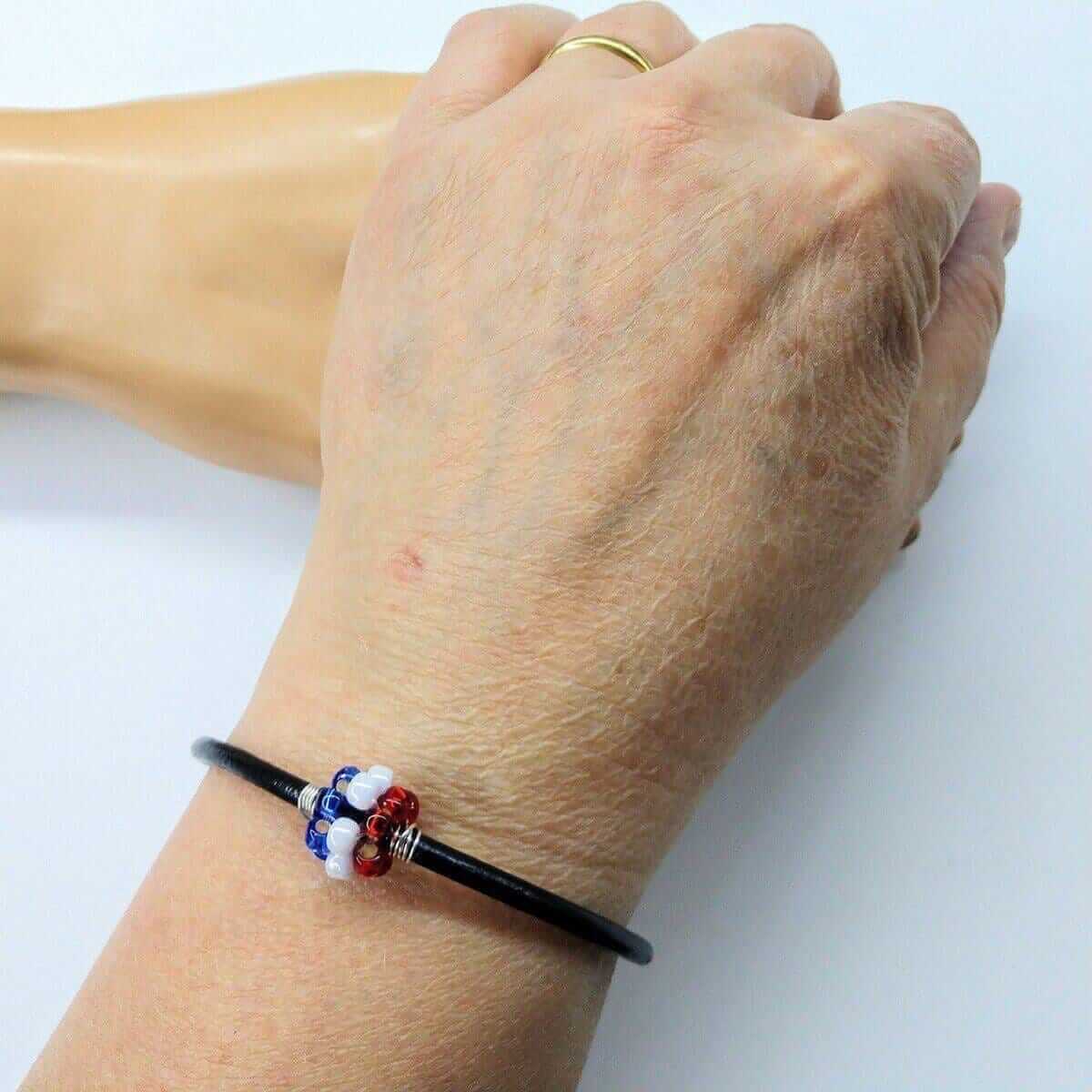 Hand wearing a bracelet with red, white, and blue beads on a light background