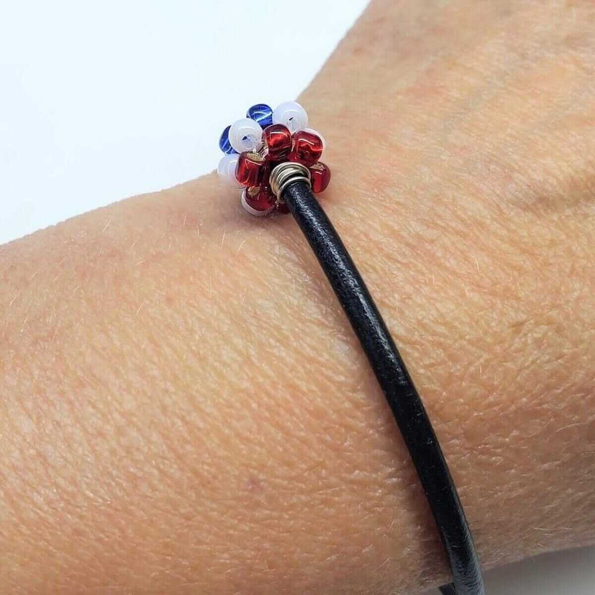 Black leather bracelet with red, white, and blue beads on a wrist against a white background