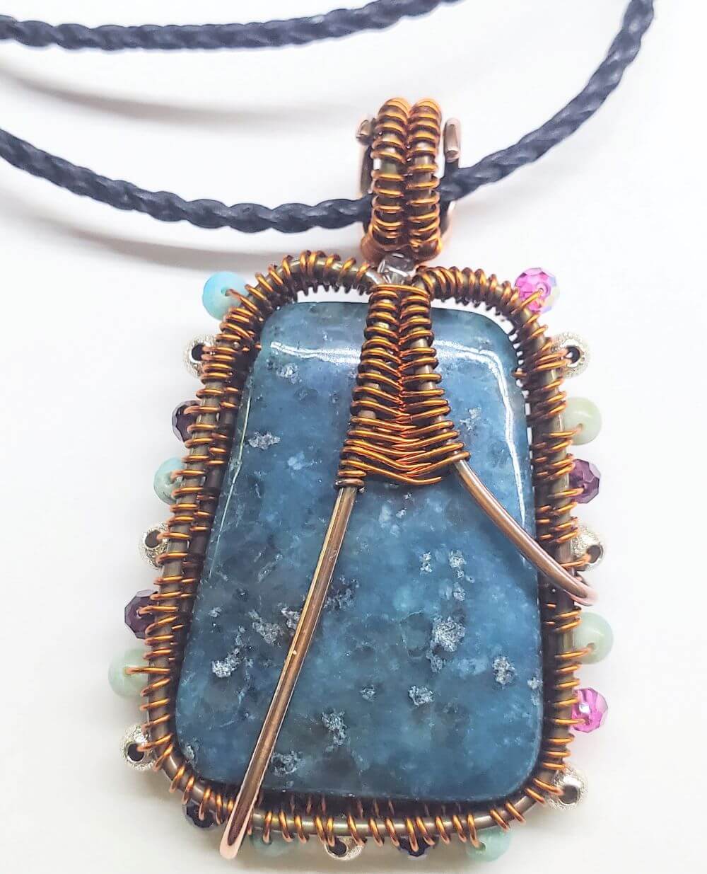 Blue stone pendant with copper wire wrapping on a white background