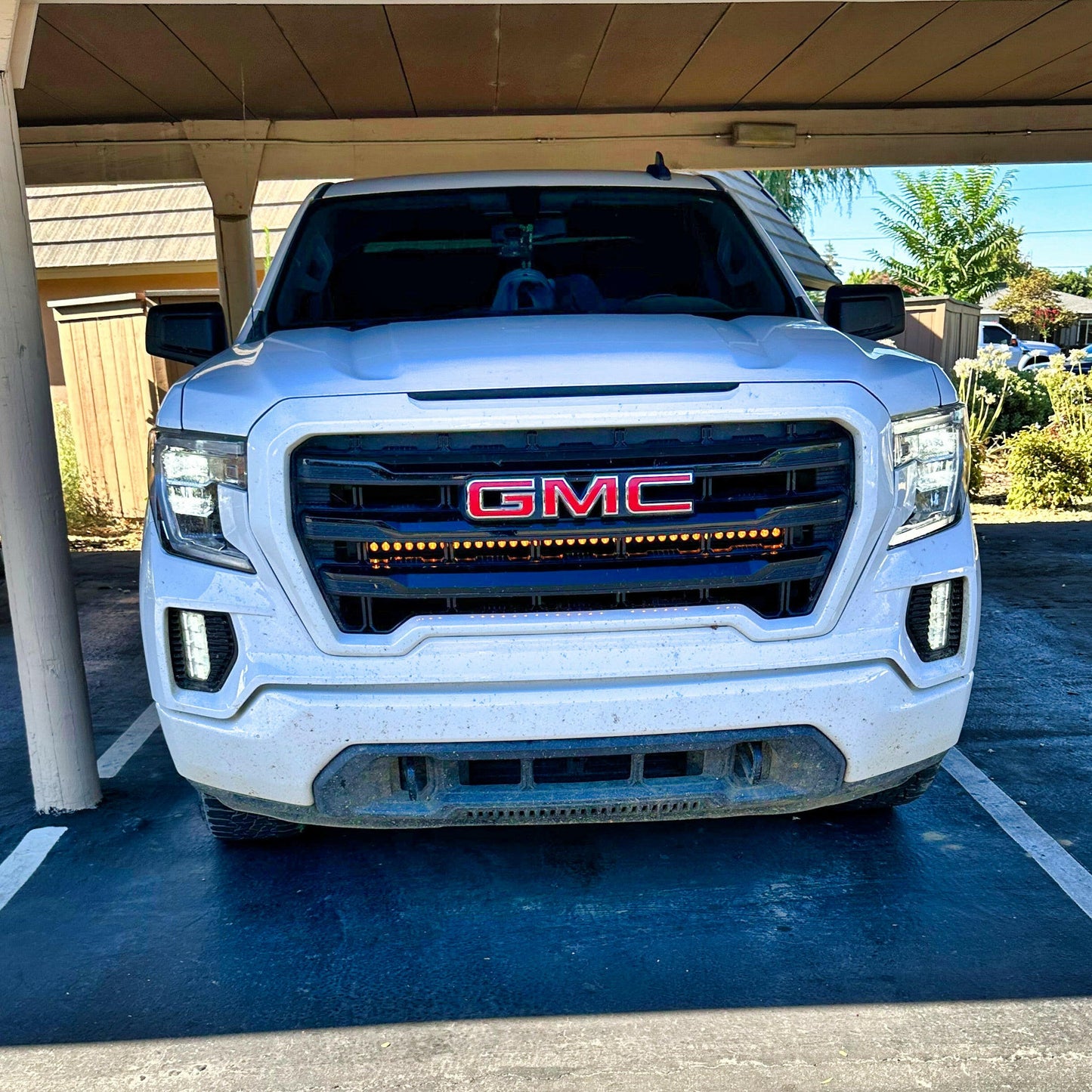 White GMC truck with LED Light Bars parked under a carport with a clear sky in the background