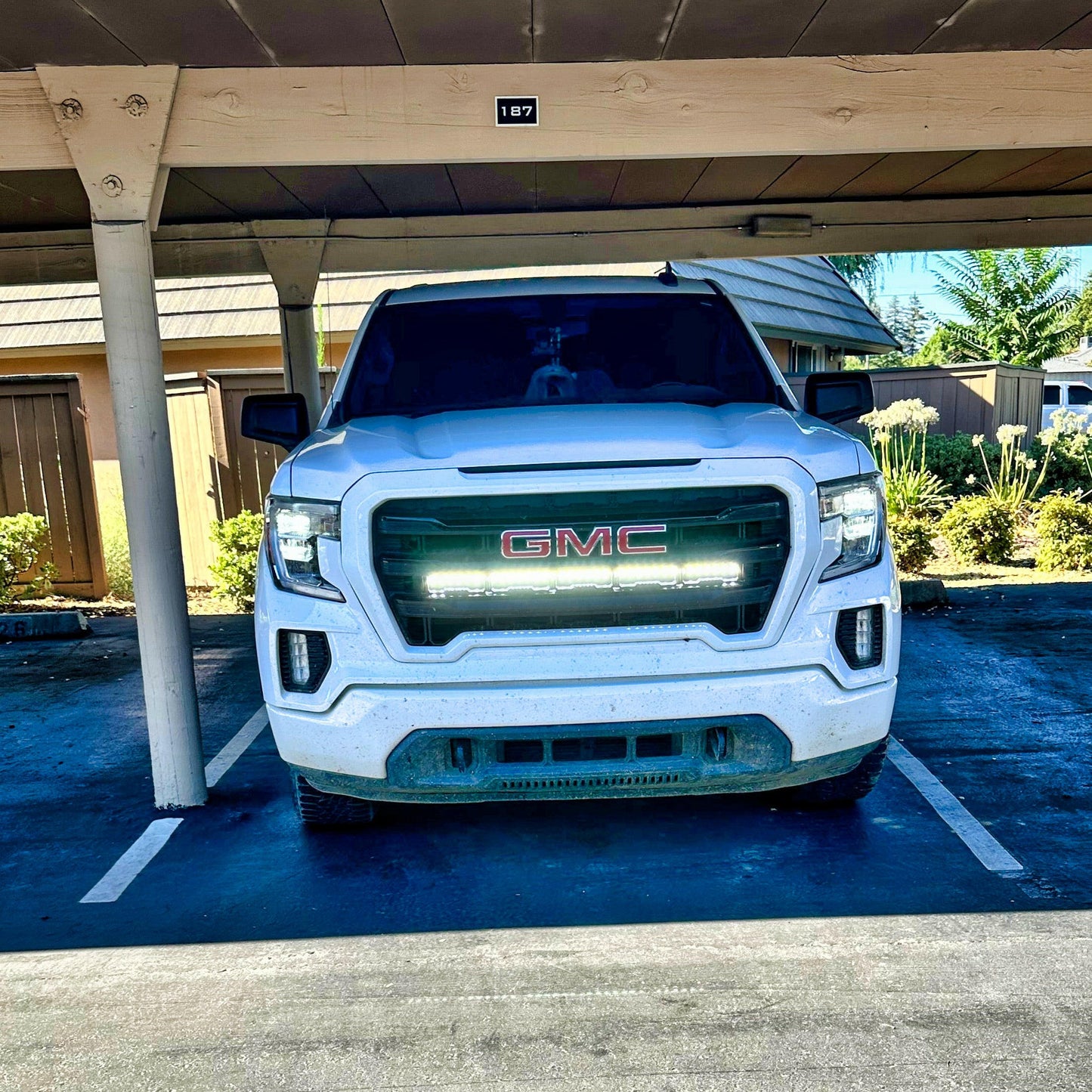White GMC truck with LED Light Bars parked under a carport with a clear sky.