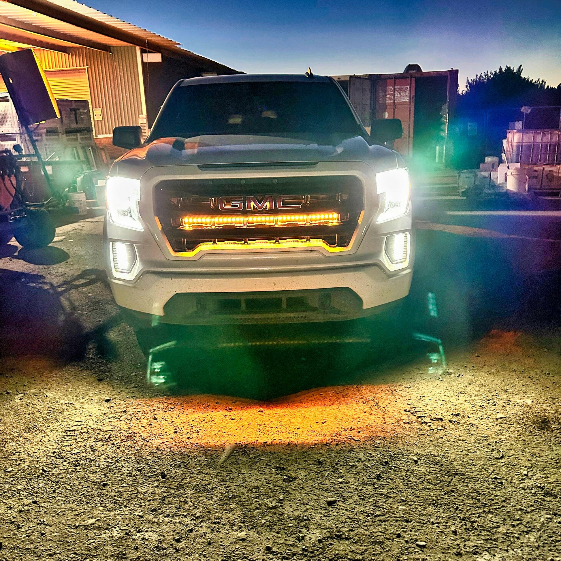 White GMC truck with LED  with light Bars illuminated front lights on a gravel surface at night