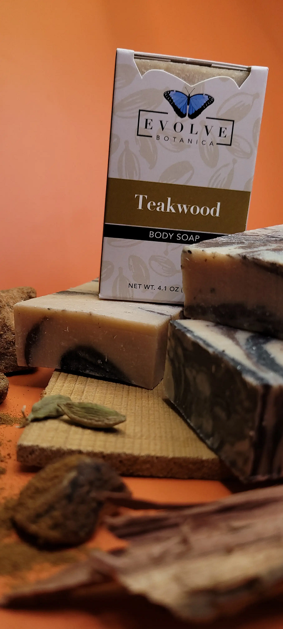 Box of Teakwood body soap by Evolve with soap bars and leaves on a wooden board.