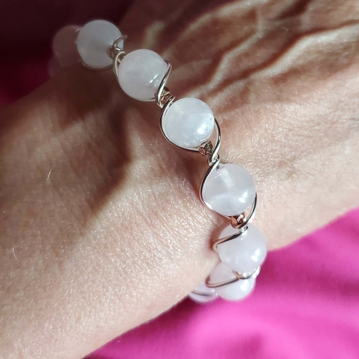 Bracelet with white beads and gold accents on a wrist against a pink fabric background