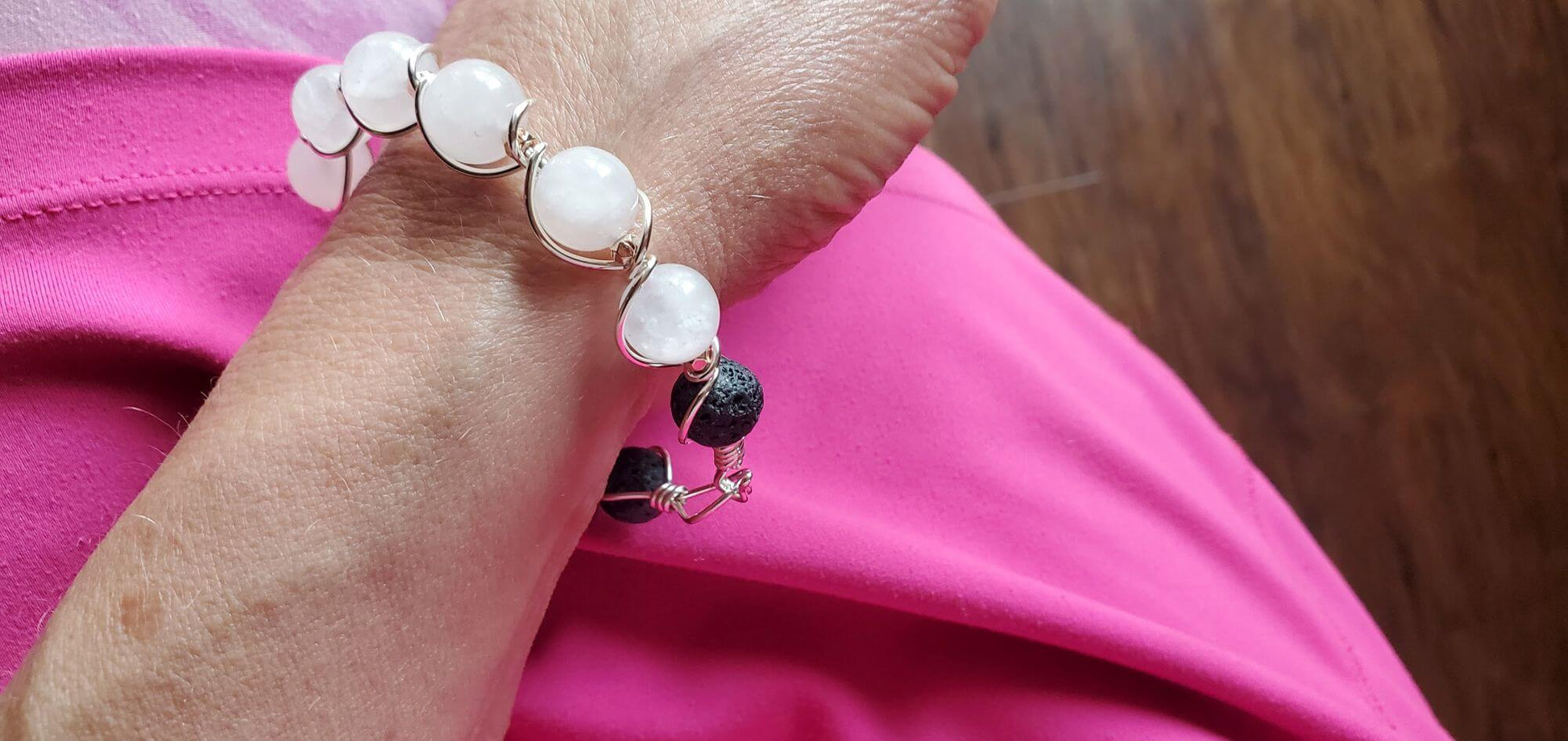 Close-up of a wrist wearing a bracelet with white beads and a black bead, against a pink background.