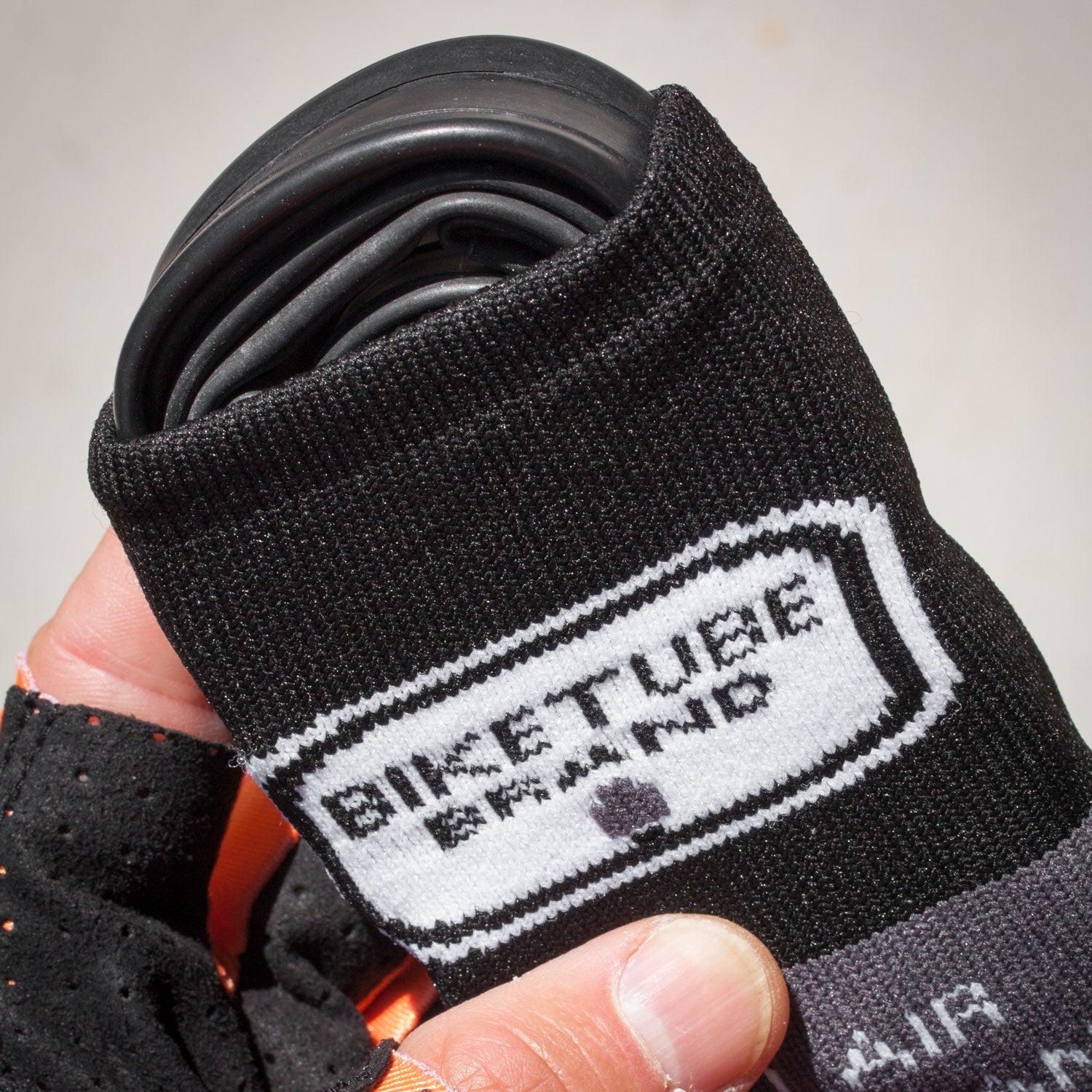 Black bike tube with 'Biketube Brand' label held by a hand against a neutral background