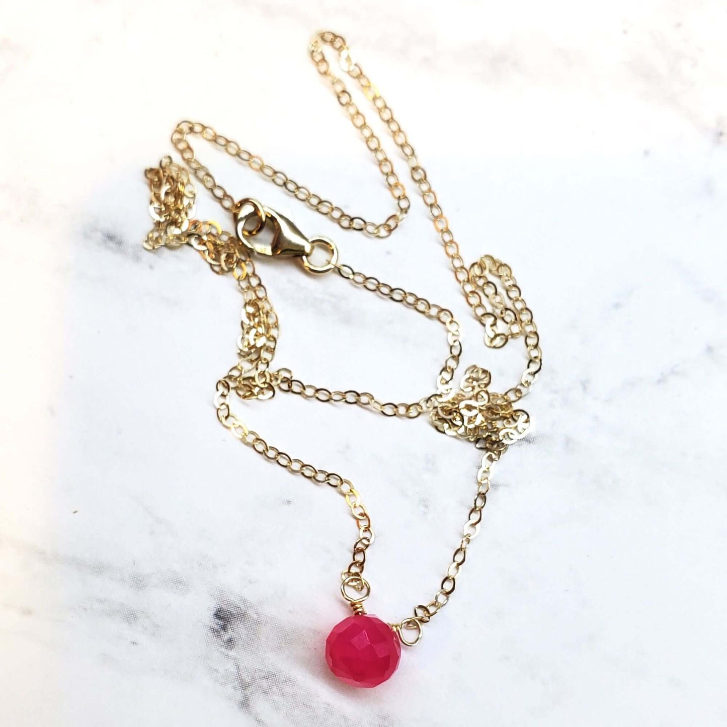 Gold necklace with a pink pendant on a marble surface