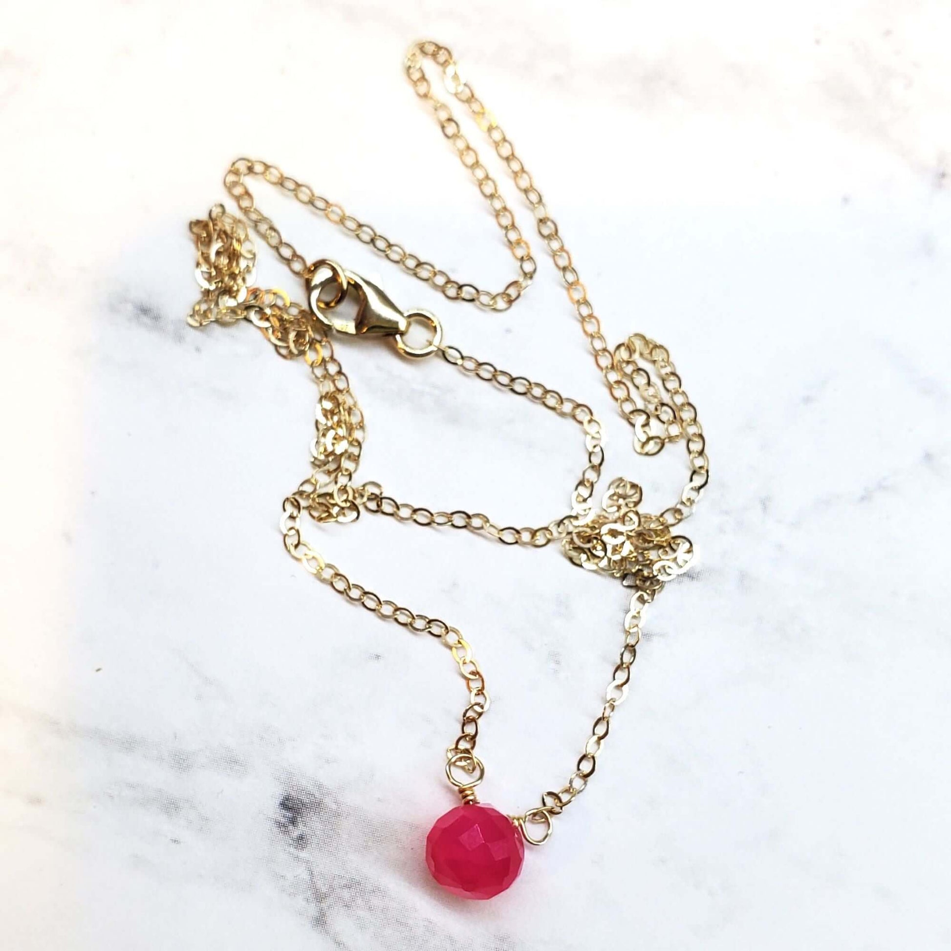 Gold necklace with a pink pendant on a marble surface