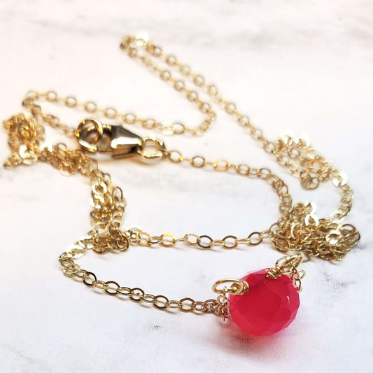 Gold chain necklace with a pink pendant on a white marble surface