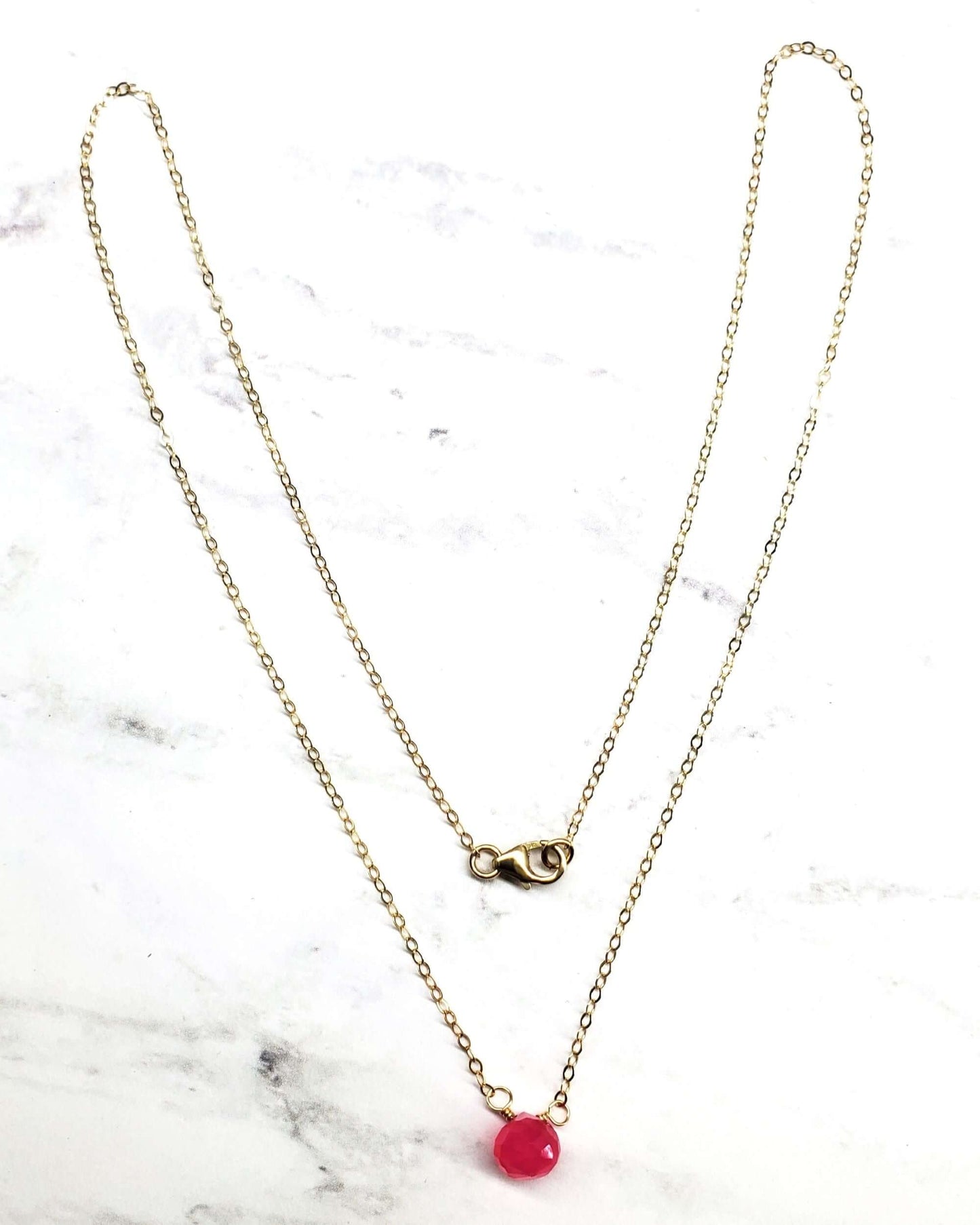 Gold necklace with a red pendant on a marble background