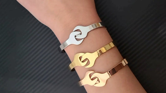 Three metallic wrench shaped bracelets on a wrist against a dark background