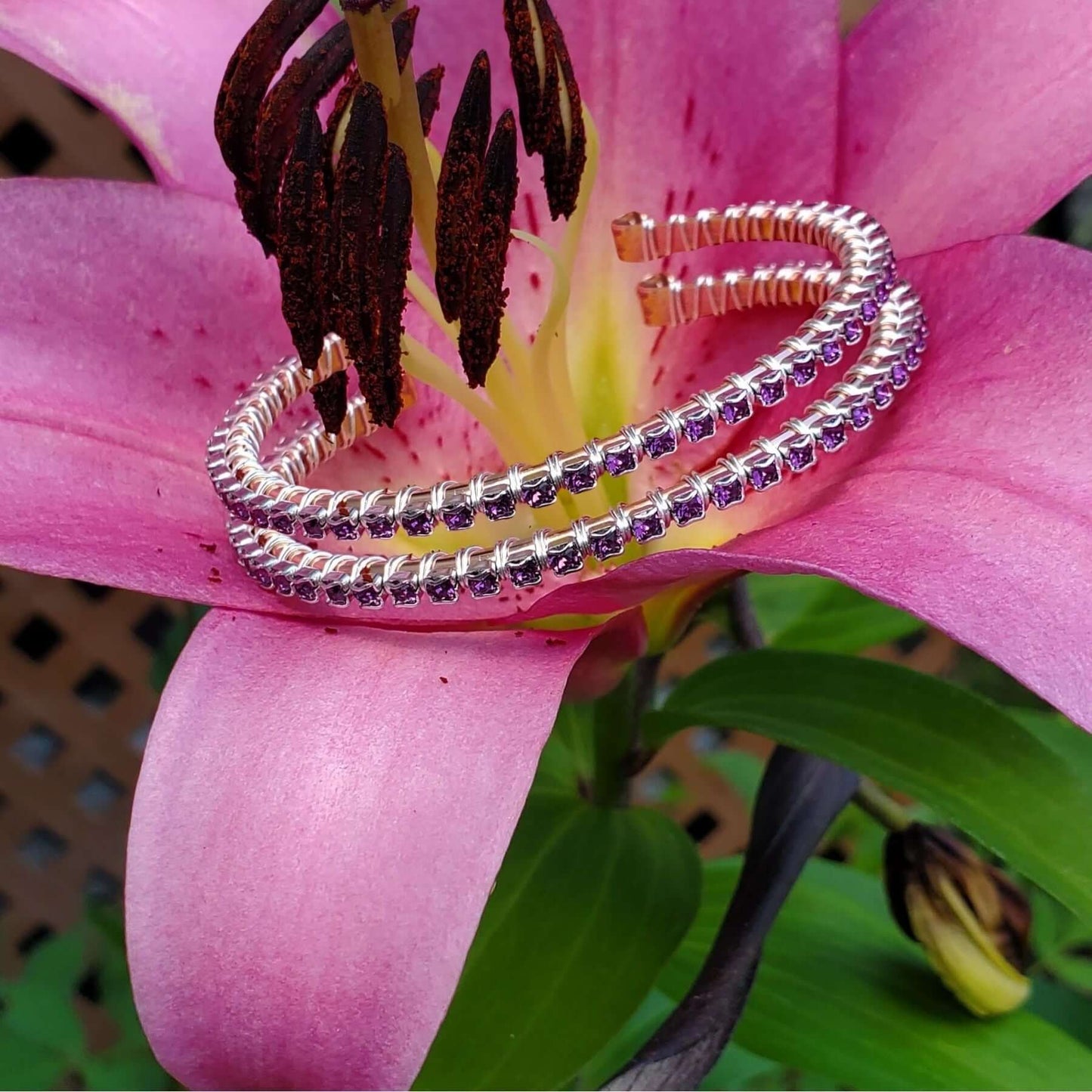 Stack of silver bracelets with purple stones on a pink lily floweret